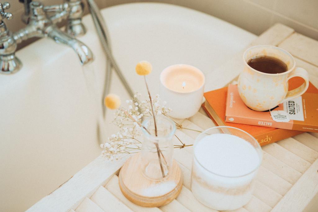 Books, warm drinks, and candles are placed next to a running bath.