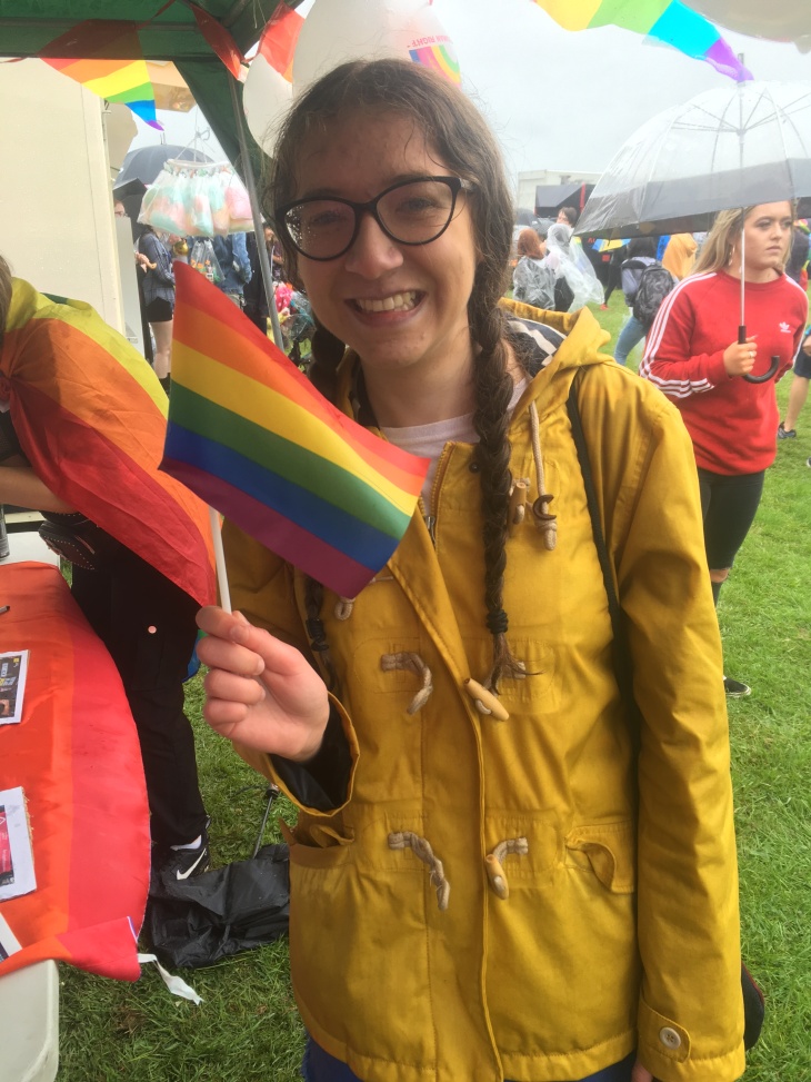 Young girl holds a Pride flag, wearing a bright yellow rain coat