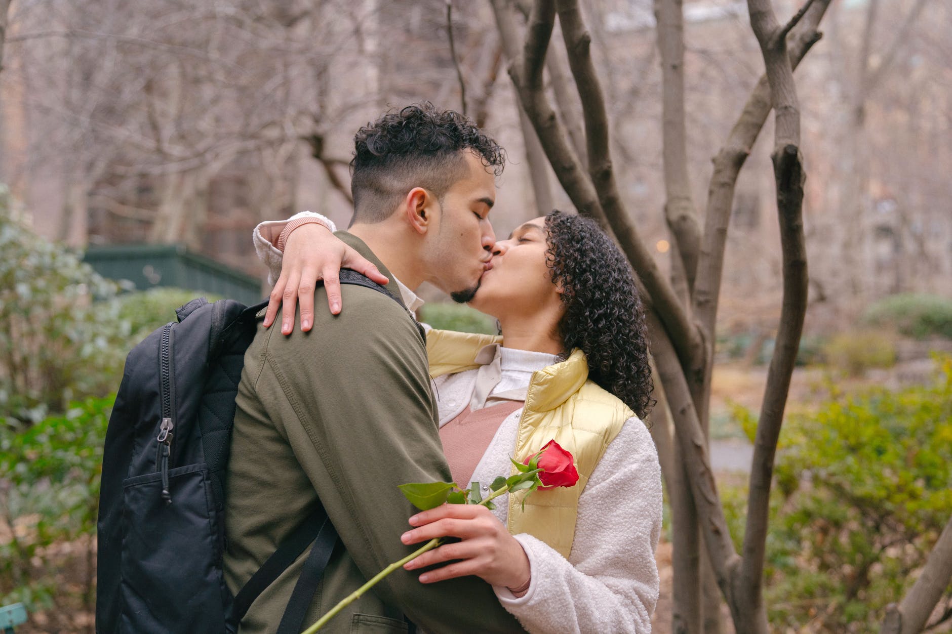 Two people kiss. The woman is holding a rose.
