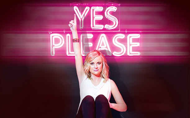 Image of Amy Poehler under neon lights that read "yes Please"